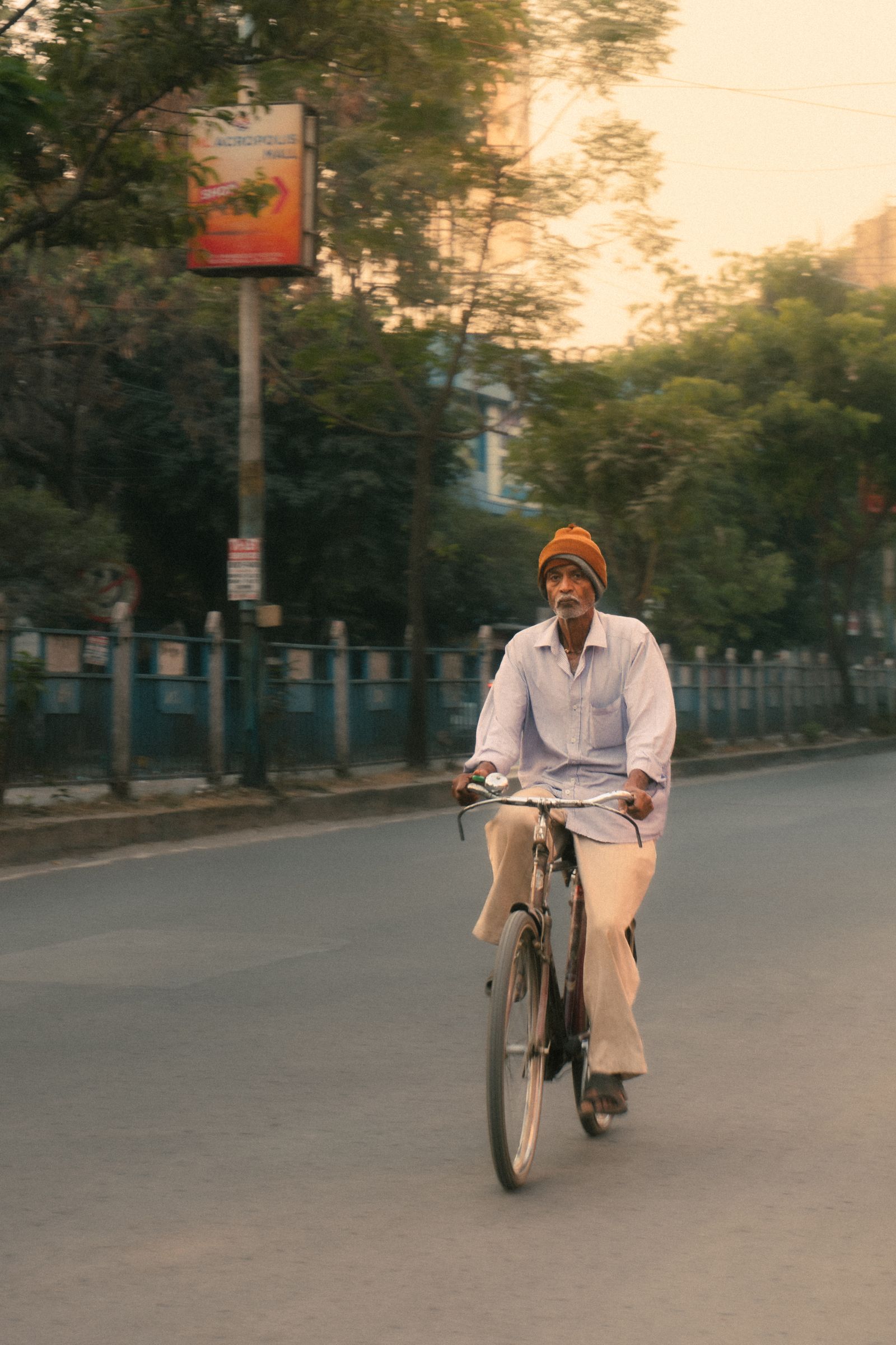 A man in his sixties cycling with energy down a tree-lined street.